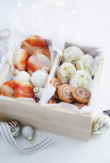 Biscuits with various icing in wooden gift box with christmas baubles — Stock Photo