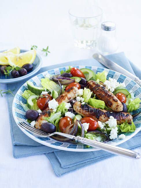 Греческий салат с сосисками подается на тарелке со столовыми приборами — стоковое фото