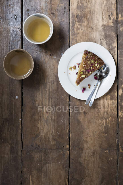 Pistachio cake with rose petals and two cups of tea on a wooden table — Stock Photo