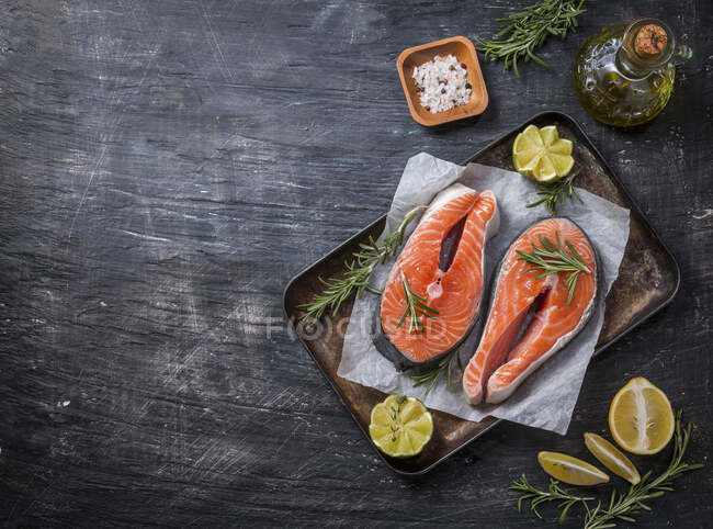 Two fresh raw salmon steaks on paper with salt, peppers, lemon, and rosemary — Stock Photo