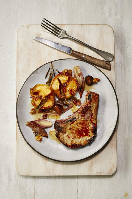 Pork chop with roast apples on plate with cutlery at wooden board — Stock Photo