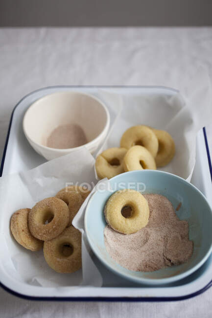 Baked mini vanilla doughnuts being dipped in cinnamon sugar — Stock Photo
