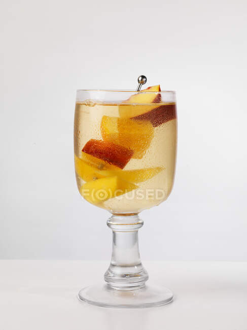 Sangria with sliced peach on metal stick in glass — Stock Photo