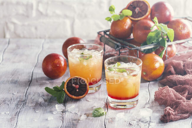 Alcohol tequila cócteles de salida del sol con naranjas rojas, hielo y menta - foto de stock