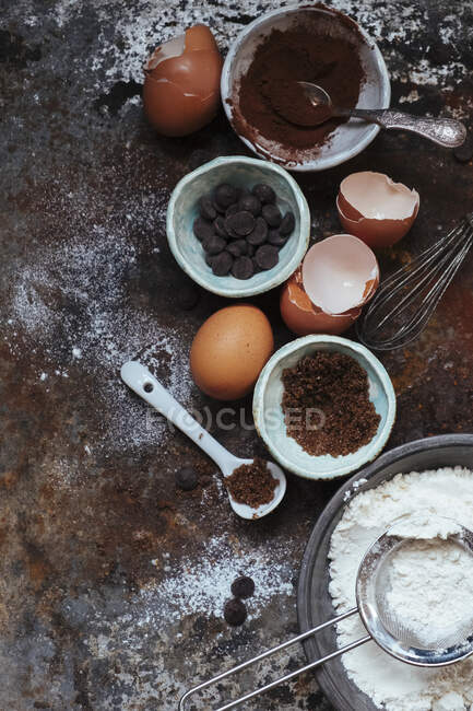 Un arreglo de utensilios para hornear: cacao, chispas de chocolate, huevos, harina y azúcar - foto de stock