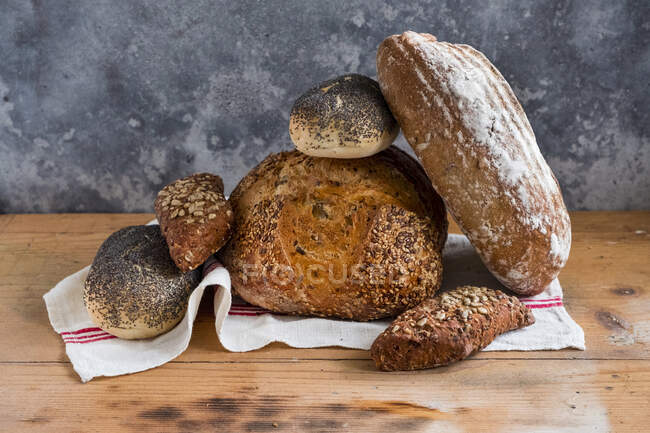 Varios panes de pan con tela en la superficie de madera - foto de stock