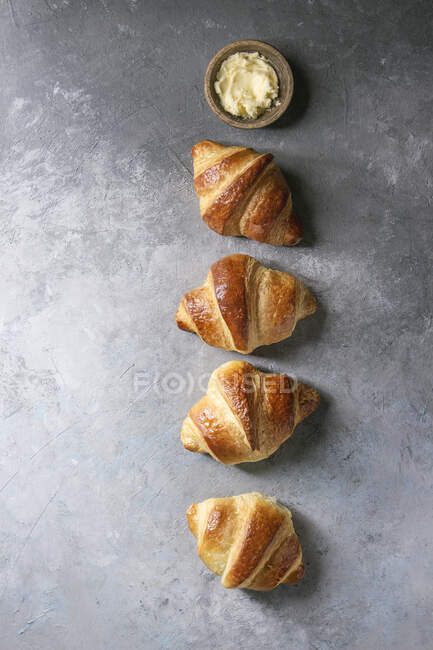 Croissant tradicional recién horneado con mantequilla en fila sobre fondo de textura gris - foto de stock
