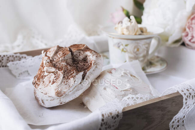 Pastel colored meringues and teacup with flowers in wooden tray — Stock Photo