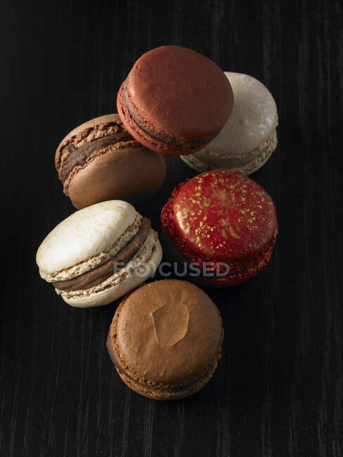 Macarons vermelhos, brancos e de chocolate no fundo escuro — Fotografia de Stock