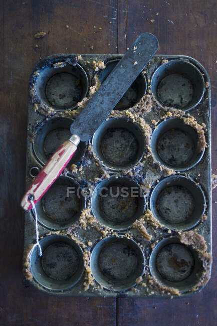 Uma lata de muffin vazia com migalhas de bolo e uma faca de paleta — Fotografia de Stock