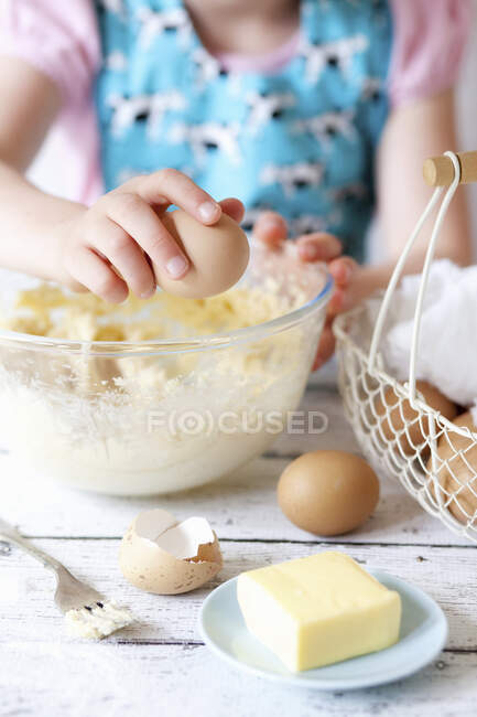 Kind knackt Eier in Rührschüssel — Stockfoto
