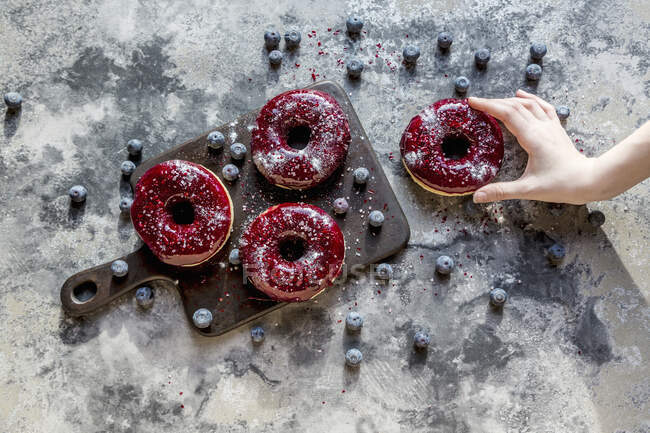 Eine Hand nimmt einen Donut mit Blaubeerglasur und Glitzerpuder — Stockfoto