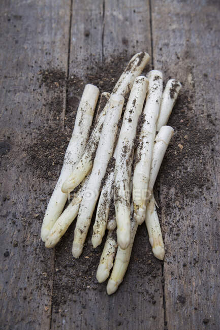 White asparagus with soil on a wooden background — Stock Photo