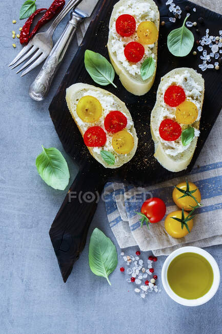 Close up of homemade tomato and basil bruschetta or sandwiches with ingredients on light grey background — Stock Photo