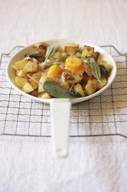 Fried potatoes with eggs and sage in pan on rack — Stock Photo