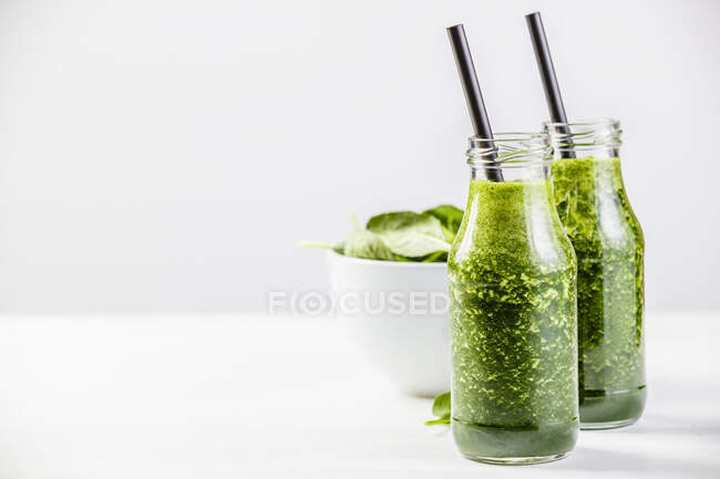 Grüner Smoothie und weiße Spinatschüssel auf weißem Tisch — Stockfoto