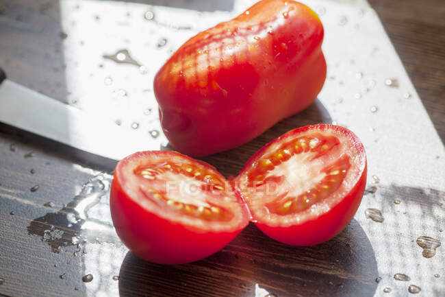 Eine ganze und eine halbierte Tomate auf einem sonnigen Tisch im Freien — Stockfoto