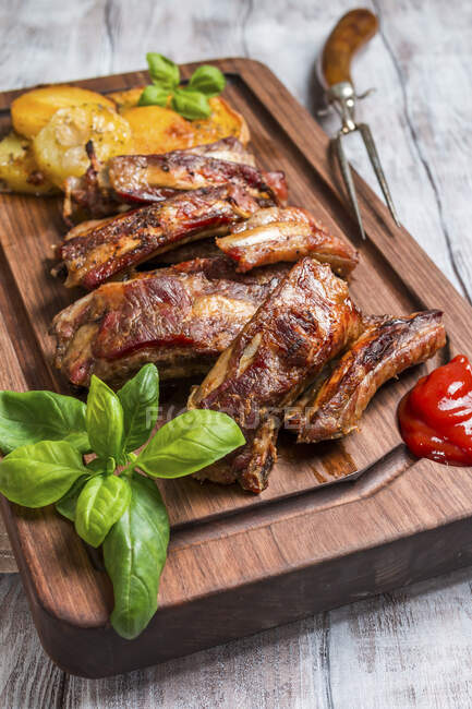 Delicious Grilled Pork Ribs and Fried Potatoes with Sauce on wooden cutting board — Stock Photo