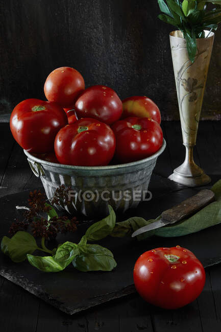 Naturaleza muerta con tomates frescos de bistec y albahaca sobre fondo negro - foto de stock