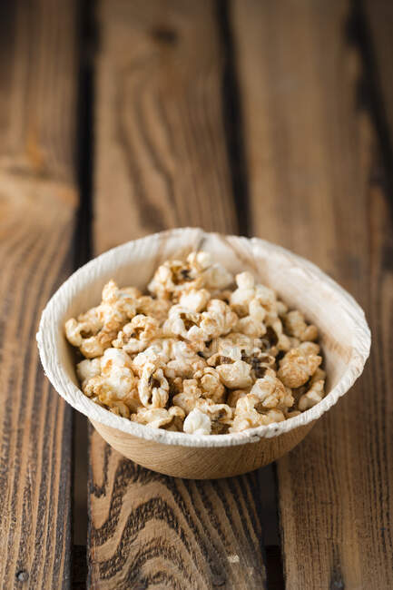 Gilded popcorn in a bowl on a wooden surface — Photo de stock