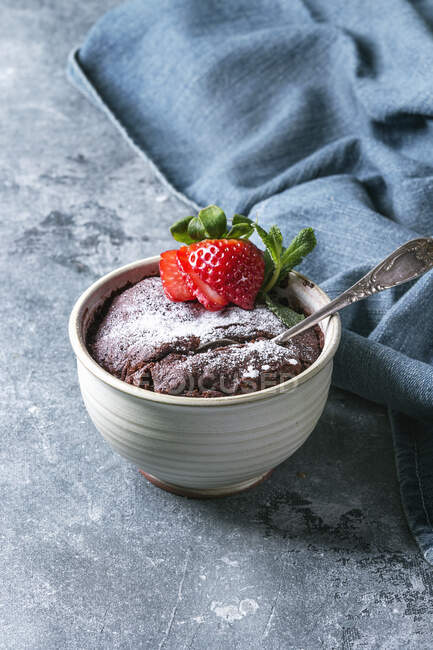 Chocolate mug cakes from microwave with strawberry and sugar powder over blue texture background - foto de stock
