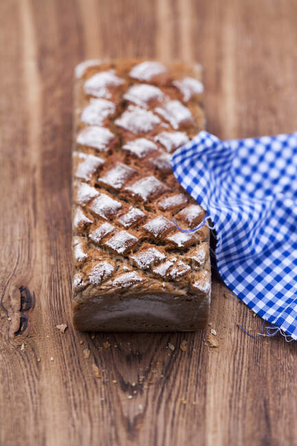 Wheat bread on wooden surface with checkered cloth — Stock Photo