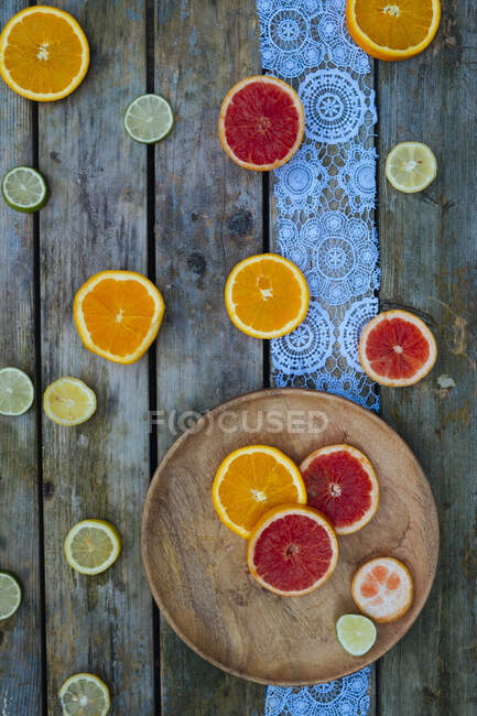 Oranges, citrons verts et tranches de pamplemousse sur plaque et surface en bois — Photo de stock