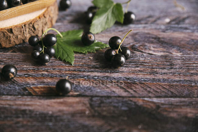 Blackcurrants with leaves on rustic wooden surface — Stock Photo