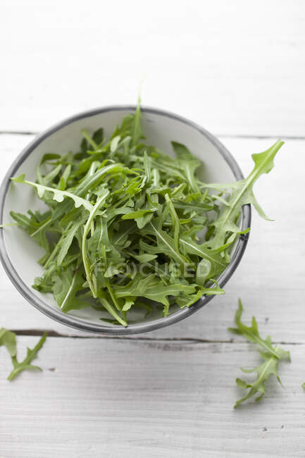 Fresh arugula in bowl on rustic wooden surface — Stock Photo