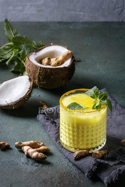 Copo de bebida ayurvédica leite de coco dourado açafrão gelado latte com curcuma em pó, hortelã e ingredientes — Fotografia de Stock