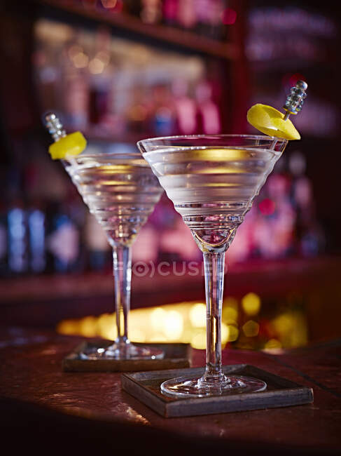 Due Martini in Twist bicchieri con scorza di limone su bastoncini di metallo al bancone del bar — Foto stock