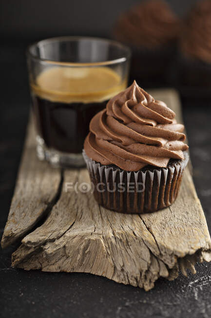 Dark chocolate cupcakes with ganache frosting on dark background with espresso in a glass — Stock Photo