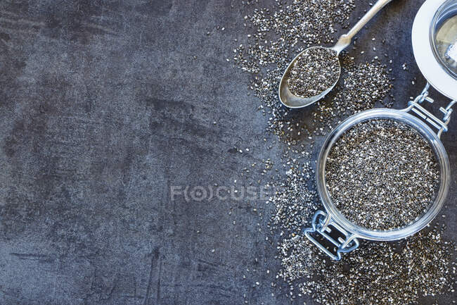 Sementes de chia em um jarro flip-top e em uma colher em uma superfície cinza (visto de cima) — Fotografia de Stock