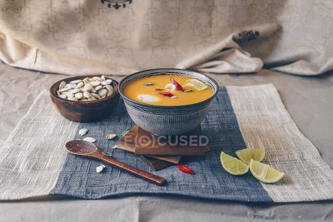 Spicy asian pumpkin soup garnished with red chillies, limes, and pumpkin seeds, topped with coconut cream — Stock Photo