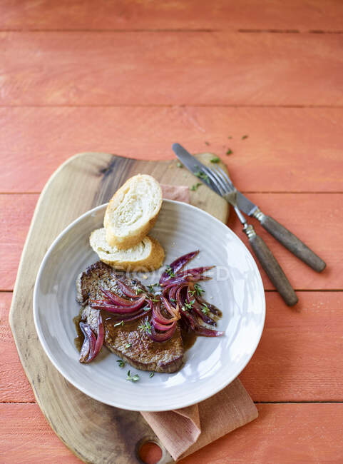 Beef steaks with balsamic onions and baguette slices — Stock Photo