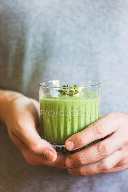 Green vegan smoothie with spinach, banana and sprouted seeds in glass in male hands — Stock Photo