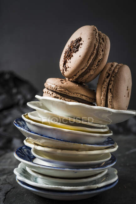 Three chocolate macaroons on stack of plates — Stock Photo