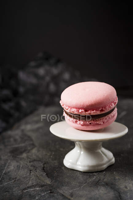 Pink macaroon with chocolate filling on mini stand — Stock Photo