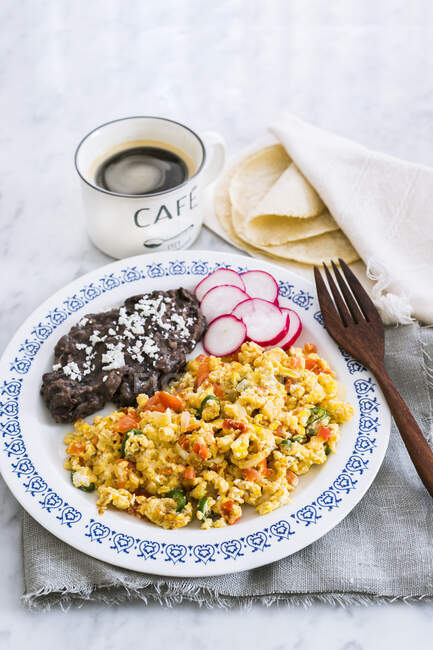 Scrambled eggs with tomatoes, onions and green chili peppers served with fried beans, tortillas and coffee in cup — Stock Photo
