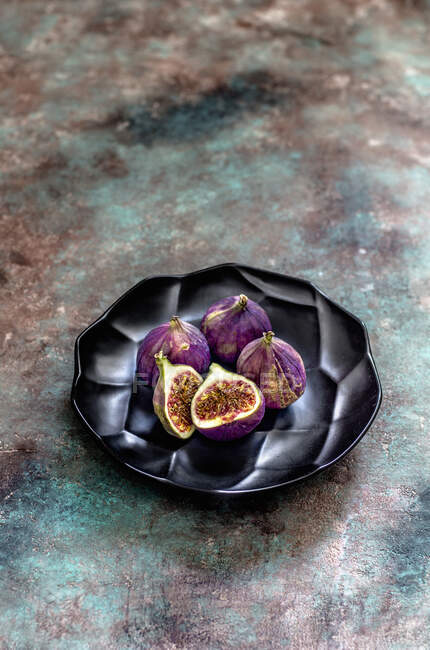Whole and halved figs on black ceramic plate — Stock Photo