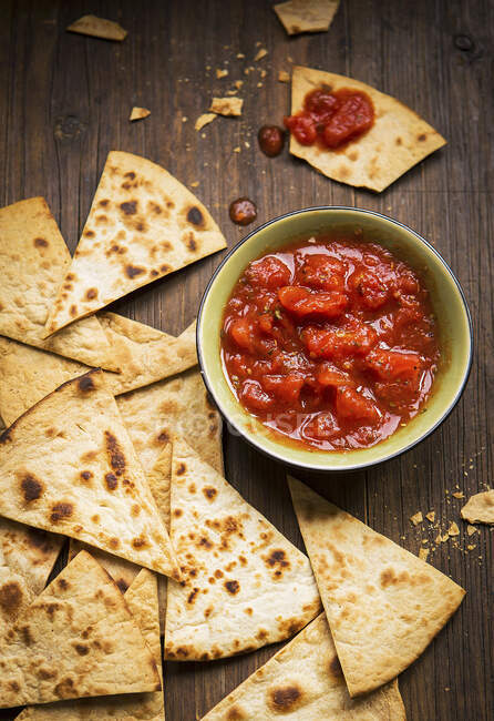 Small bowl and tomato salsa served with handmade tortilla chips on a rustic wooden board — Stock Photo