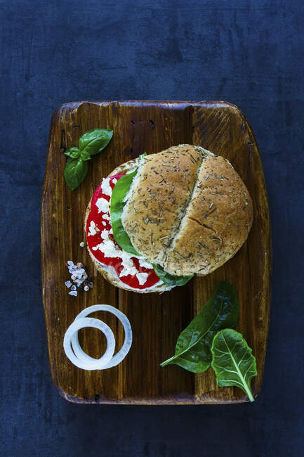 Healthy vegetarian sandwich with feta cheese, tomatoes, basil and pepper served on wooden chopping board over vintage background — Stock Photo