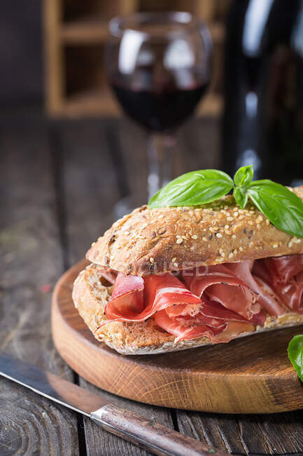 Закройте сэндвич с чиабаттой с хамоном серрано и базиликом, на деревянном фоне — стоковое фото