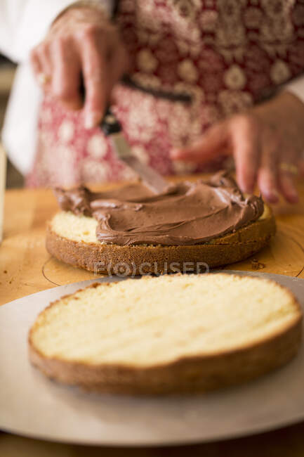 Um bolo sendo feito: creme de chocolate sendo espalhado em um bolo reduzido para metade — Fotografia de Stock
