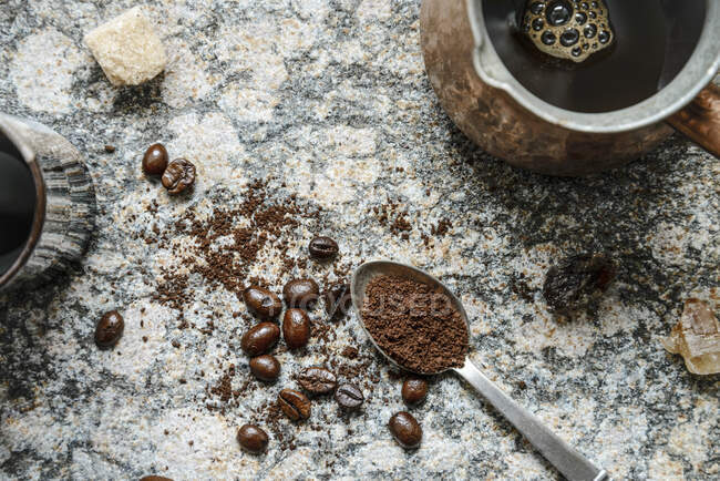 Top down view of scattered coffee beans, ground coffee in a spoon, brewed coffee in jezva on a granite surface — Stock Photo