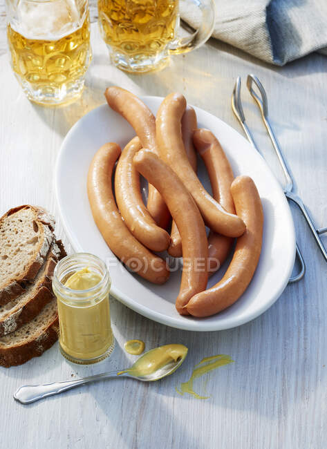 Sausages with beer tankards, a jar of mustard and bread — Stock Photo