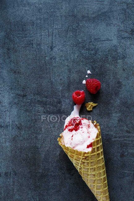 Малиновое мороженое в конусе на голубой серой поверхности — стоковое фото