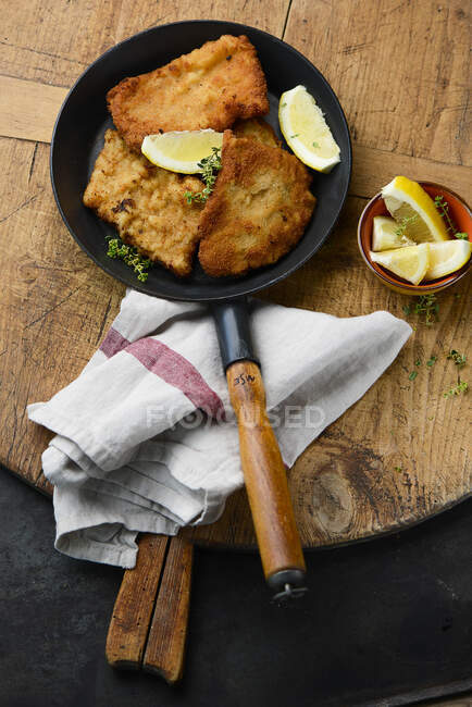 Breaded pork schnitzels in pan with lemon wedges — Stock Photo