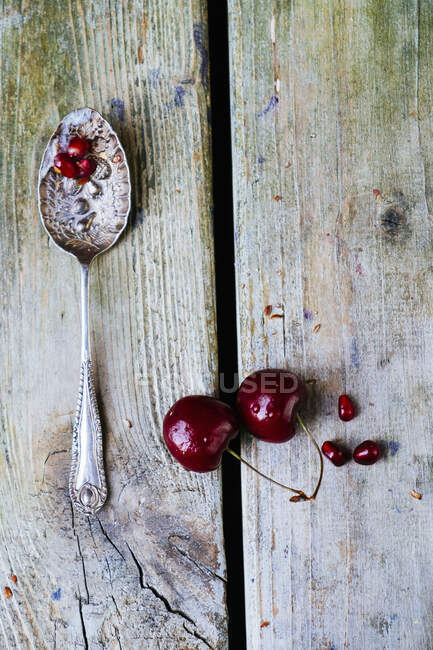 Cherries, pomegranate seeds and old spoon on wooden background — Stock Photo
