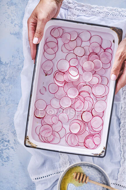 A woman holding a tray of radish slices in water — Stock Photo
